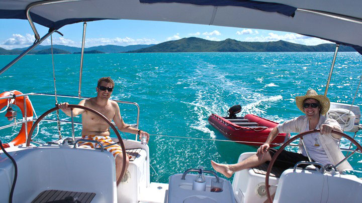 Two men sailing a vessel and towing a dinghy in the Whitsundays